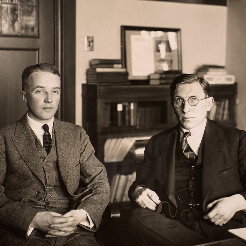 Original black and white photograph. Shows Best and Banting seated in an office, formally posed. Both men are wearing three piece suits.