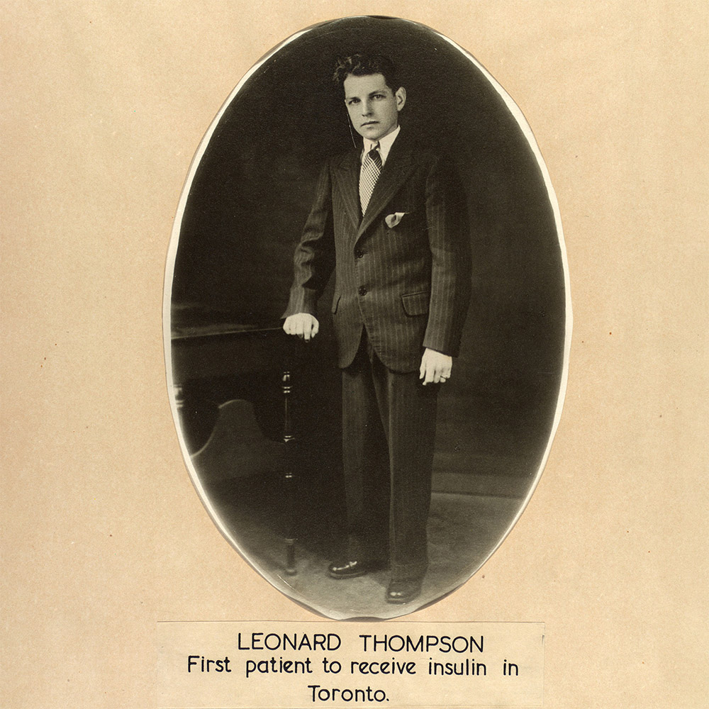 Full length photograph showing Leonard Thompson as a young man standing with one hand resting on a table.